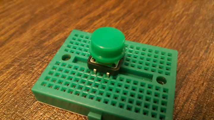 Front view of button being inserted into mini breadboard